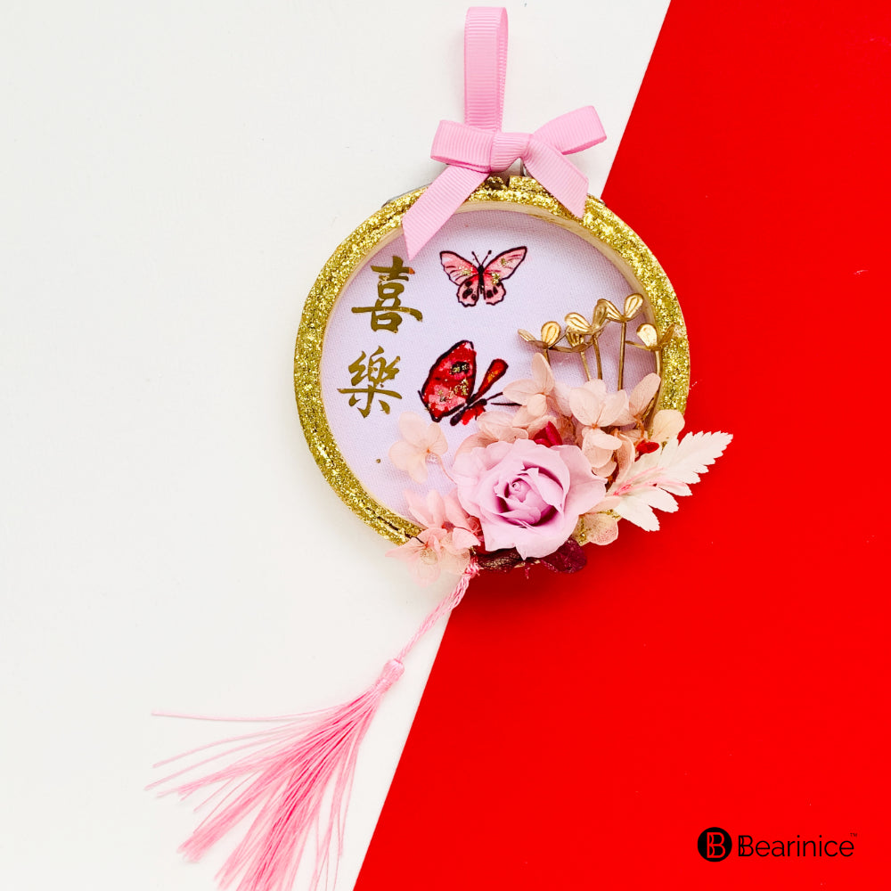 A round preserved flower ornament with a tassel, featuring a watercolor-painted fish design on fabric, accompanied by cherry blossoms and red berries, finished with a pink ribbon bow.