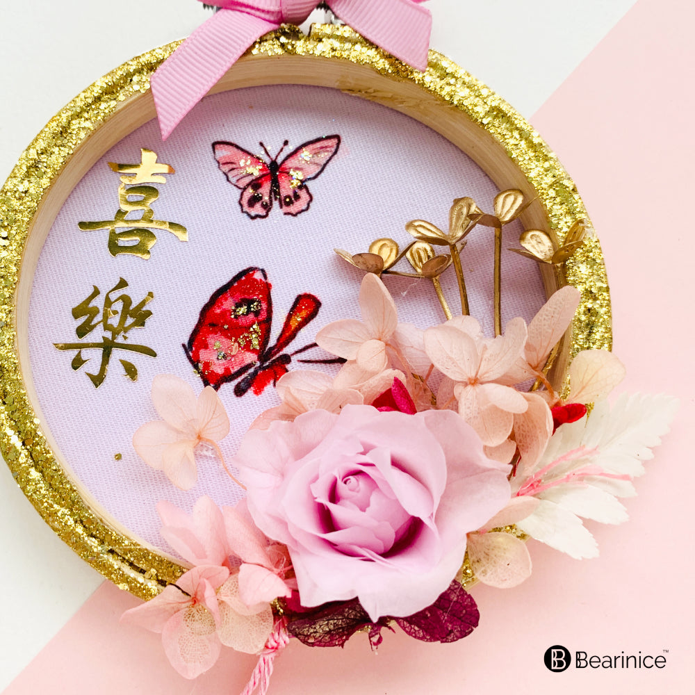 A round preserved flower ornament with a tassel, featuring a watercolor-painted fish design on fabric, accompanied by cherry blossoms and red berries, finished with a pink ribbon bow.