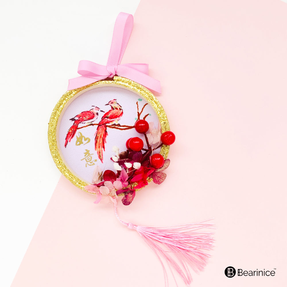 A round preserved flower ornament with a tassel, featuring a watercolor-painted fish design on fabric, accompanied by cherry blossoms and red berries, finished with a pink ribbon bow.