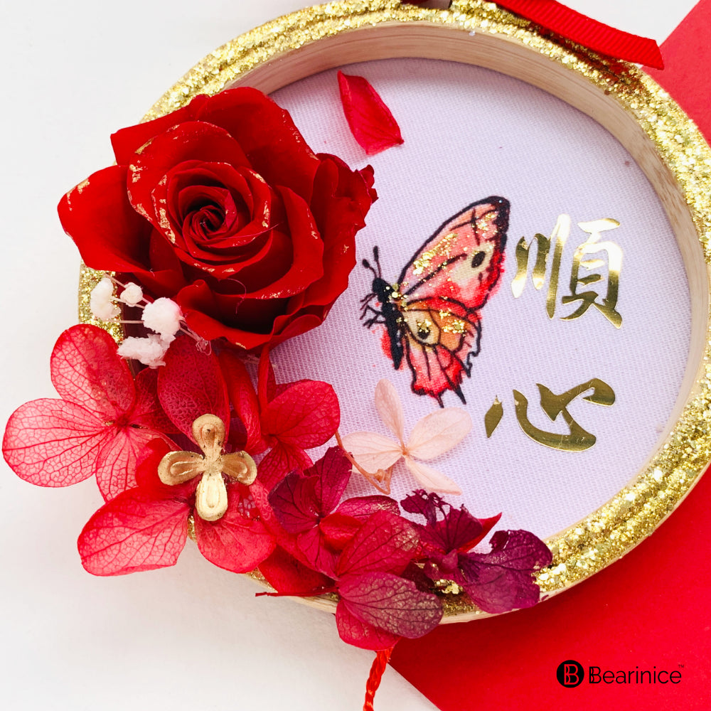 A round preserved flower ornament with a tassel, featuring a watercolor-painted fish design on fabric, accompanied by cherry blossoms and red berries, finished with a pink ribbon bow.