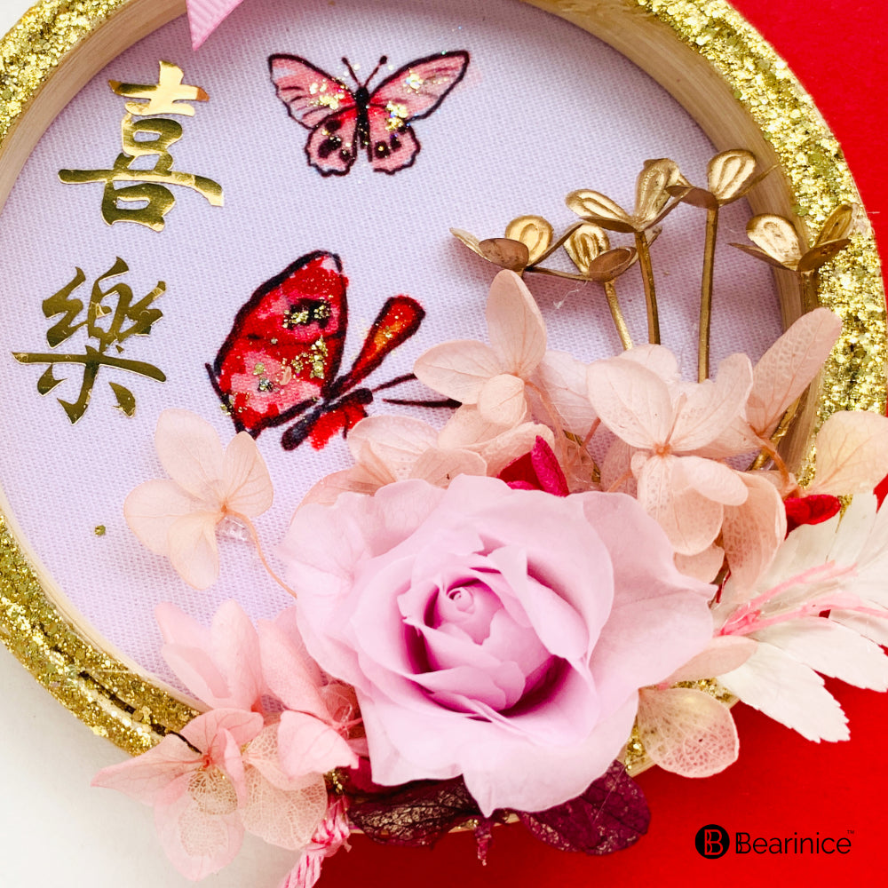 A round preserved flower ornament with a tassel, featuring a watercolor-painted fish design on fabric, accompanied by cherry blossoms and red berries, finished with a pink ribbon bow.